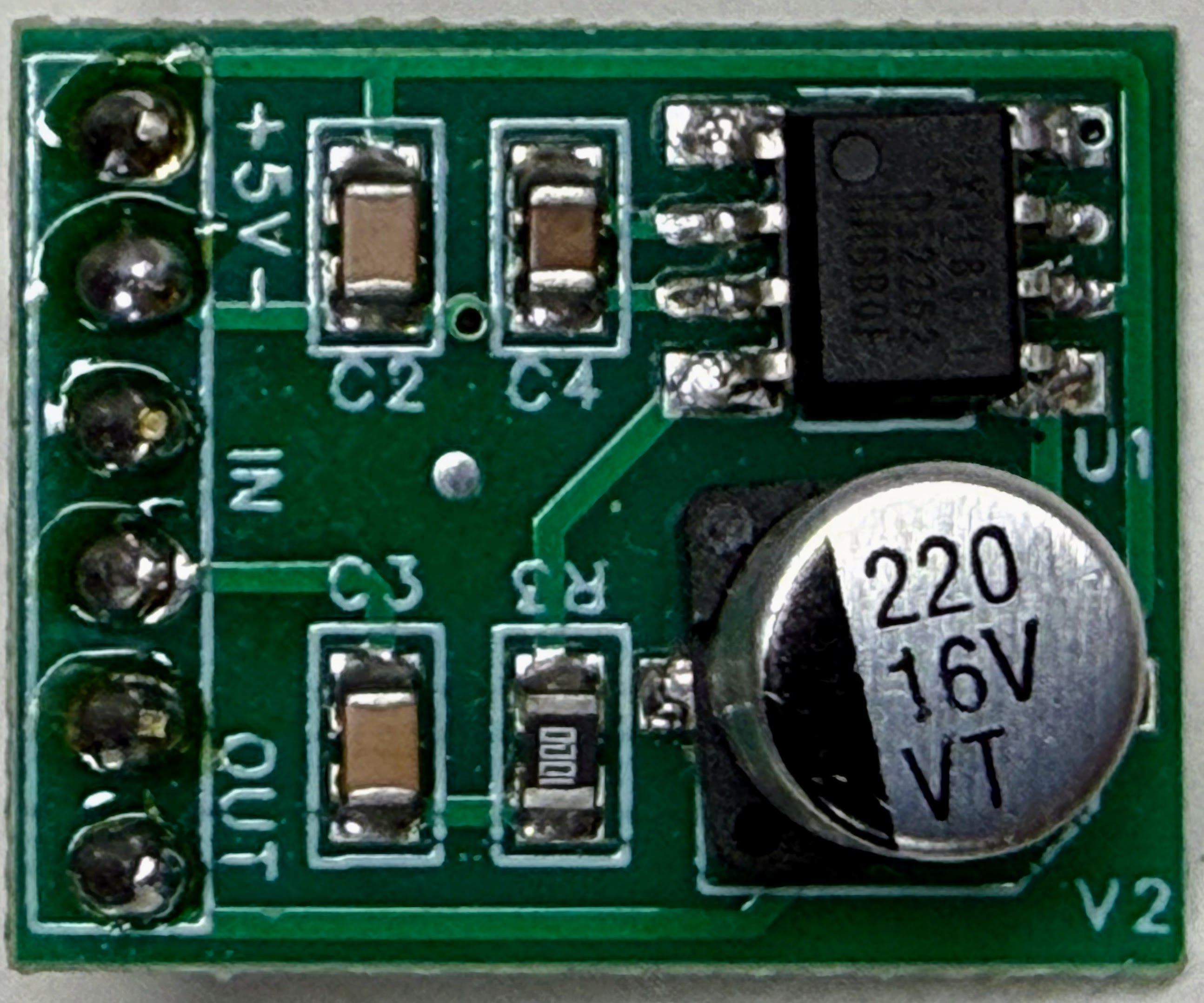 Top view of a small green XPT8871 amplifier board. Six holes run down the left edge in three labelled pairs: plus 5 V and minus at the top, IN in the middle, and OUT at the bottom. The black eight-pin amplifier chip is marked U1, and a silver 220 microfarad 16 volt capacitor sits beside it. Small surface-mount parts are marked C2, C3, C4 and R3. There is no volume knob anywhere on the board